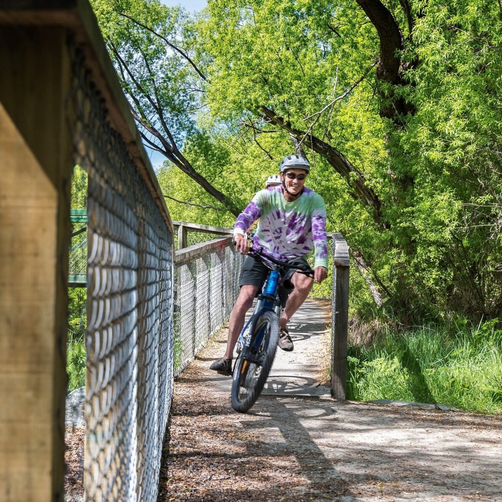 Two cyclists ride on a path through lush greenery and trees.